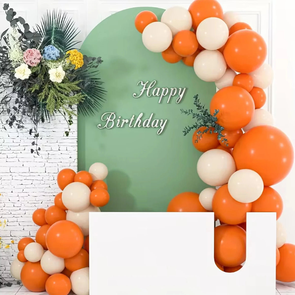 A large arrangement of orange and white latex balloons decorated with greenery against a light green background.