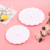 White ceramic serving plates and a glass on a pink surface with a lemon and roses.