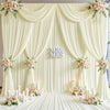 A luxurious cream fabric backdrop with draped curtains and floral accents for an event or wedding.