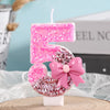 A pink glitter candle shaped like the number 5 with a bow decoration