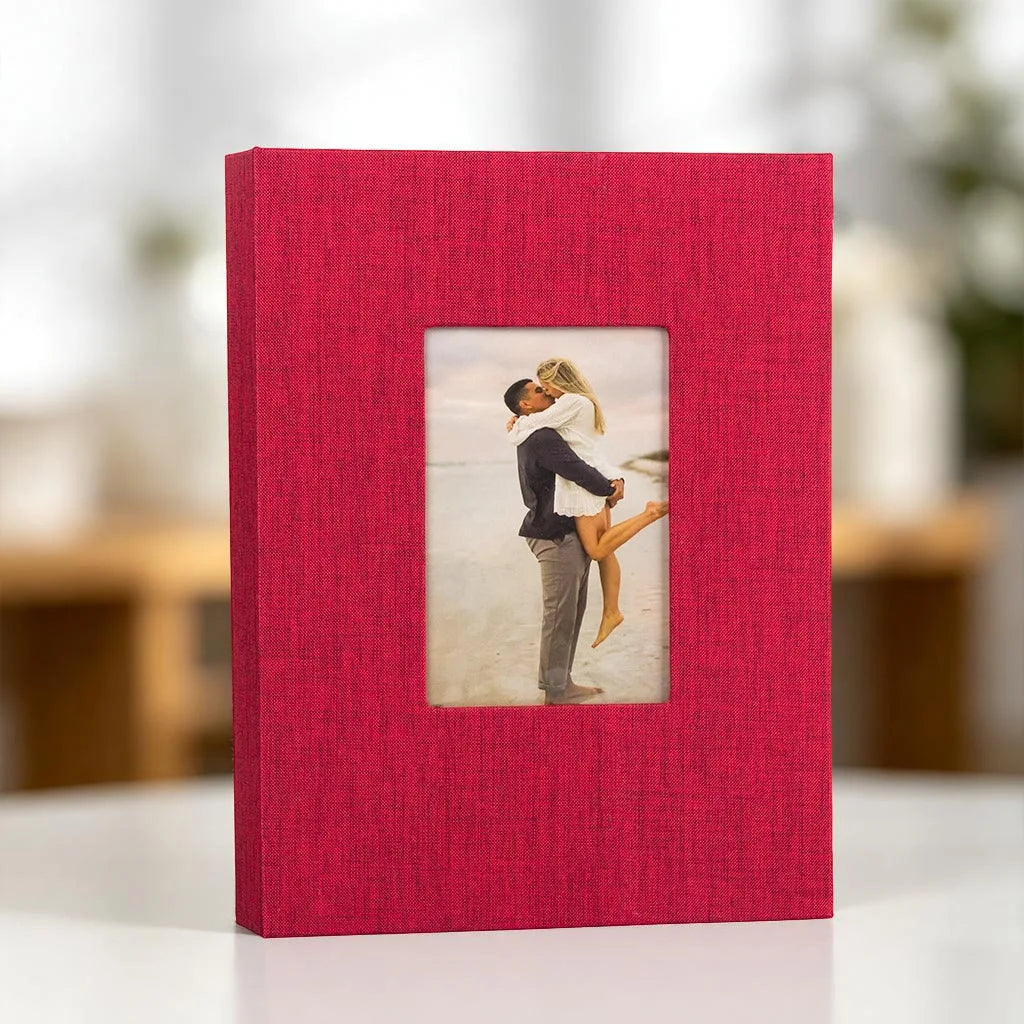 A red linen photo album with a front display window showing a couple embracing.