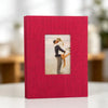 A red linen photo album with a front display window showing a couple embracing.