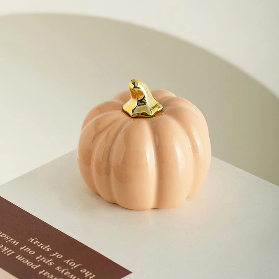 A smooth, pale peach ceramic pumpkin figurine with a gold accent sits on a white surface.