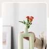 A person holds a pale green geometric ceramic vase with red roses against a light background.