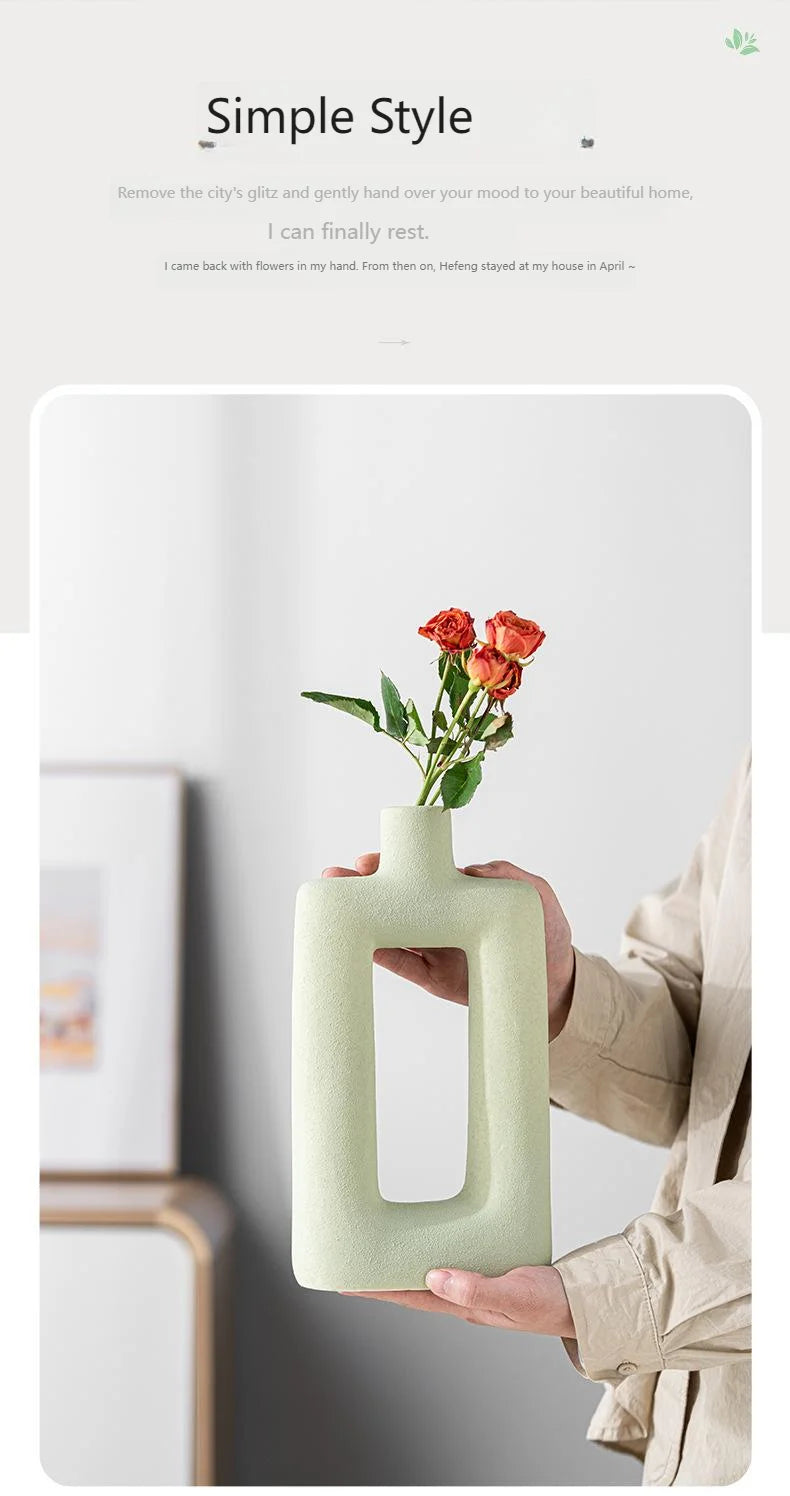A person holds a pale green geometric ceramic vase with red roses against a light background.