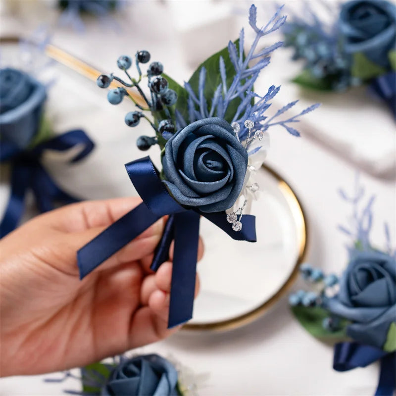 A hand holds a dusty blue silk rose boutonniere featuring blue thistle and lavender sprigs.