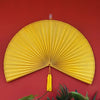 A bright yellow handwoven bamboo wall fan decor with a tassel displayed against a red background.