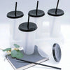 A set of clear reusable tumblers with black lids and straws displayed on a book.