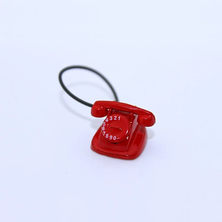 A small, vintage red rotary desk phone miniature with a black cord.