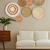 A gallery wall featuring various round woven straw and natural fiber wall hangings on a beige wall above a light sofa.