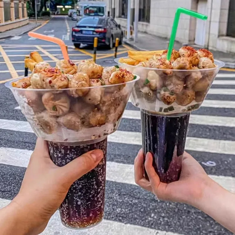 A hand holds a plastic cup filled with purple drink and fruit snacks on a crosswalk.