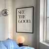 A framed black and white inspirational quote canvas featuring the text SEE THE GOOD on a light gray wall.