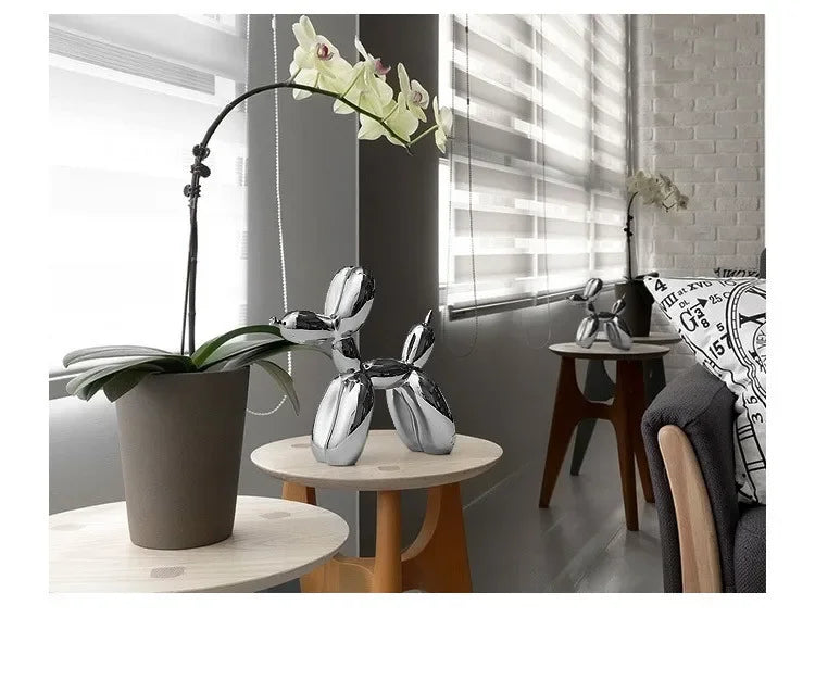 Silver resin balloon dog sculpture with a long stem and green leaves displayed on a wooden table.
