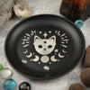 Un plat de bijoux en cristal noir décoratif avec un visage de chat blanc entouré d'étoiles et de lunes crescentes.