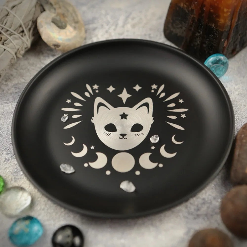 Un plat de bijoux en cristal noir décoratif avec un visage de chat blanc entouré d'étoiles et de lunes crescentes.