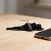 A black, draped reclining female statue sculpture is shown on a wooden desk next to a smartphone.
