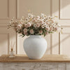 A rustic textured round vase filled with dried flowers sits on a wooden surface.