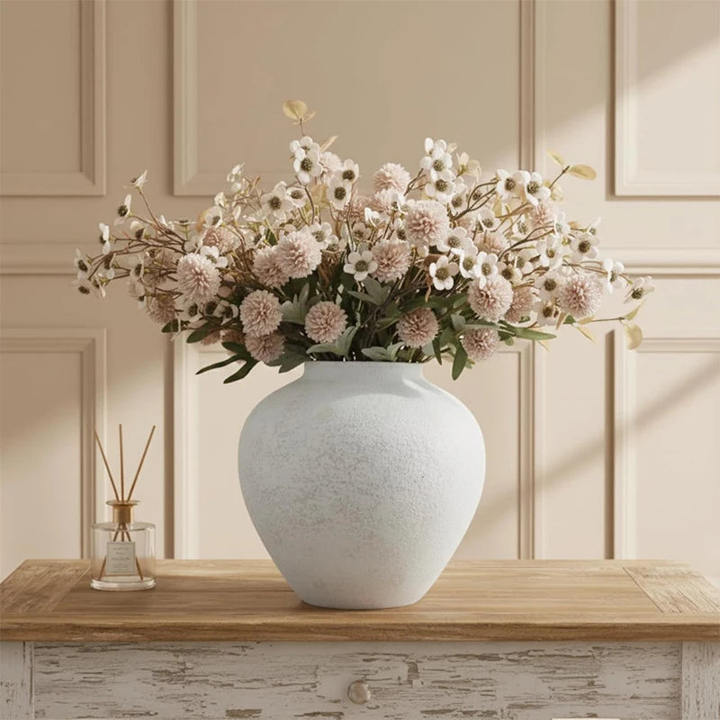 A rustic textured round vase filled with dried flowers sits on a wooden surface.