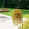 A tall metal stand holds a vibrant cascade of orange and yellow faux silk flowers in a garden setting.