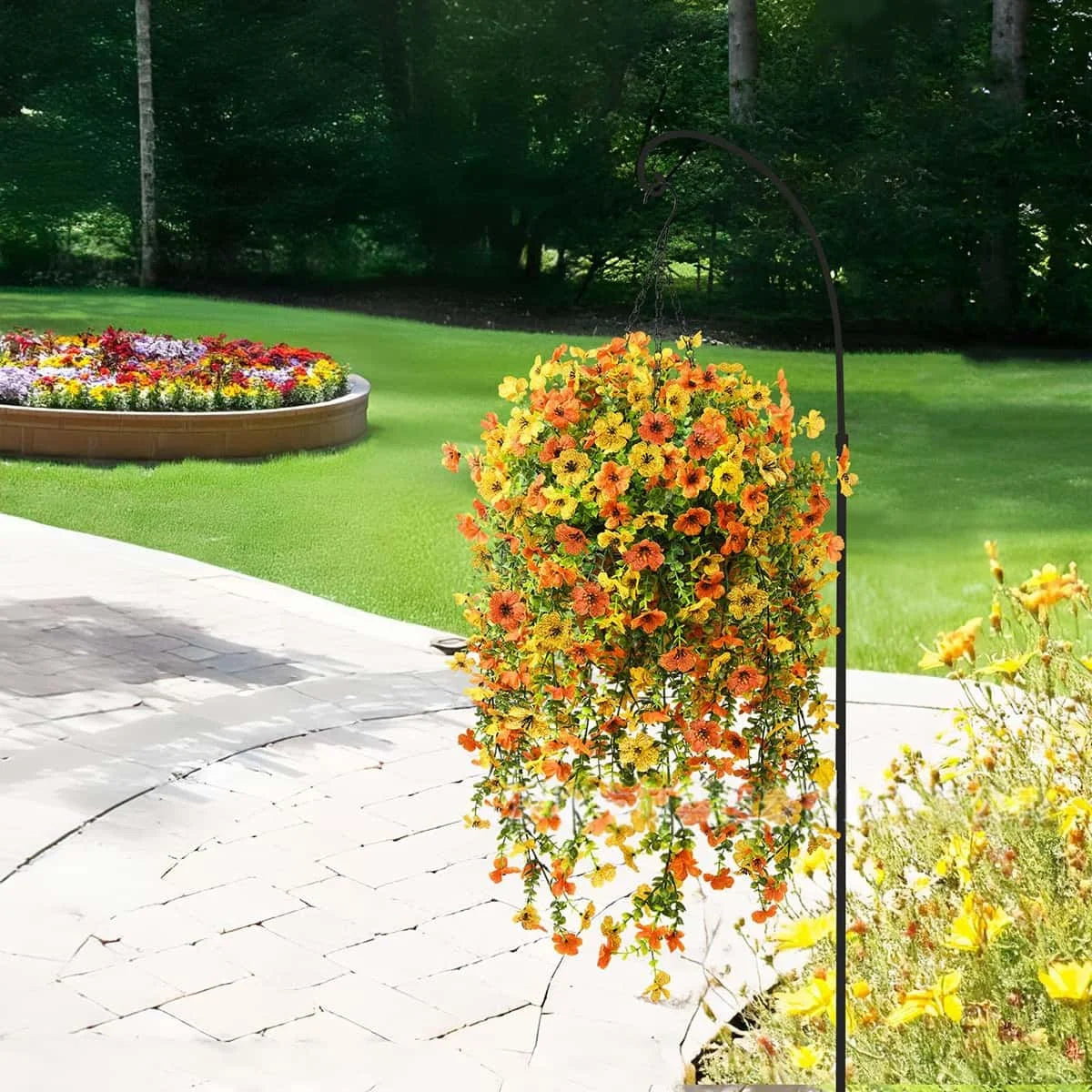 A tall metal stand holds a vibrant cascade of orange and yellow faux silk flowers in a garden setting.