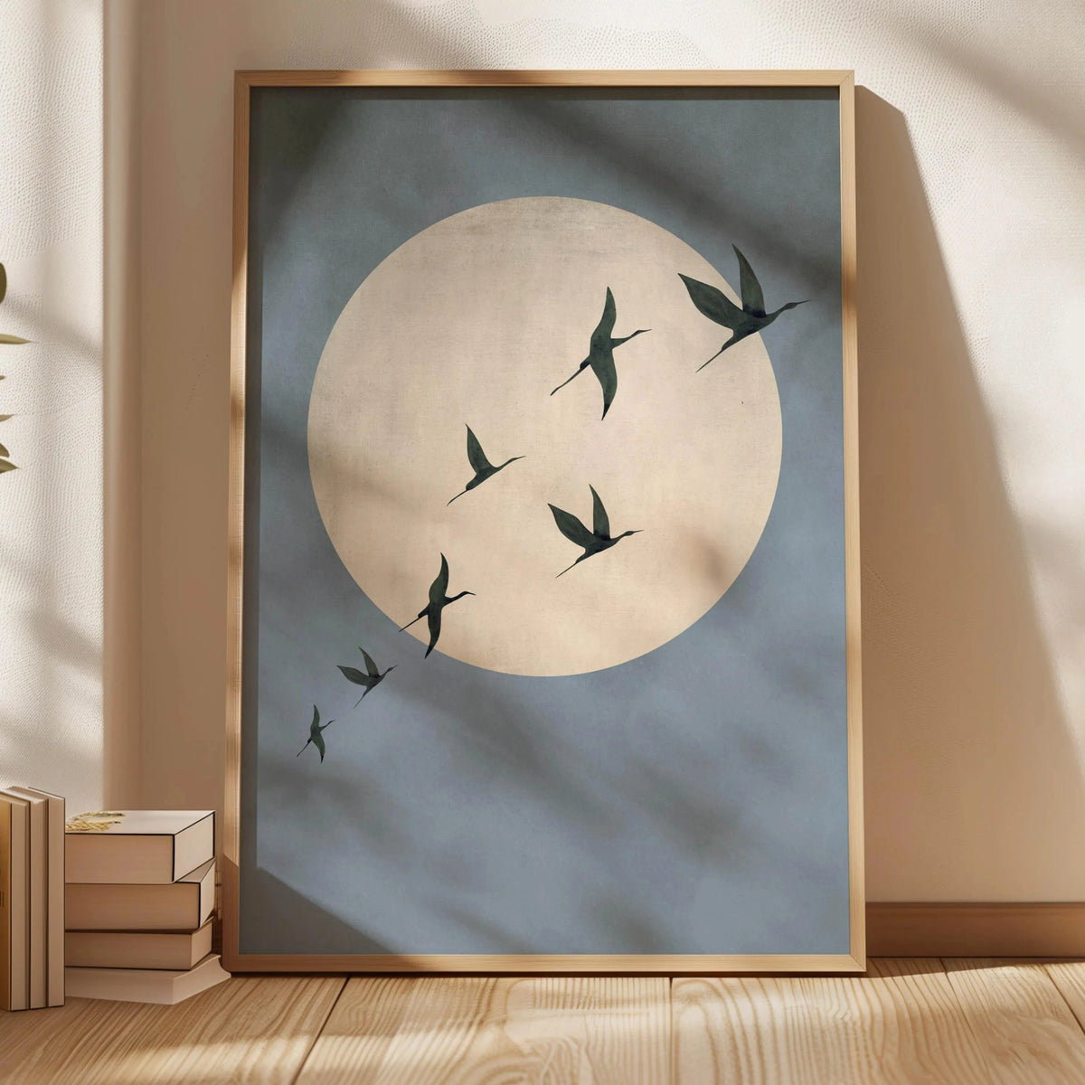 A framed canvas print featuring a large pale circle against a muted blue background with several black silhouettes of cranes 