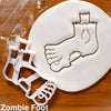 A white fondant cookie cutter shaped like a zombie foot is placed on a wooden surface.