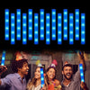 A group of four people are holding and using LED foam glow sticks in a dark setting.