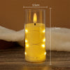 A tall glass candle holder filled with yellow wax and featuring a glowing flame and string lights.