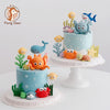 A tiered cake decorated with ocean animal toppers including a whale, octopus, and turtle.