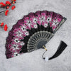 A black folding fan decorated with vibrant pink and white floral patterns on a gray background.