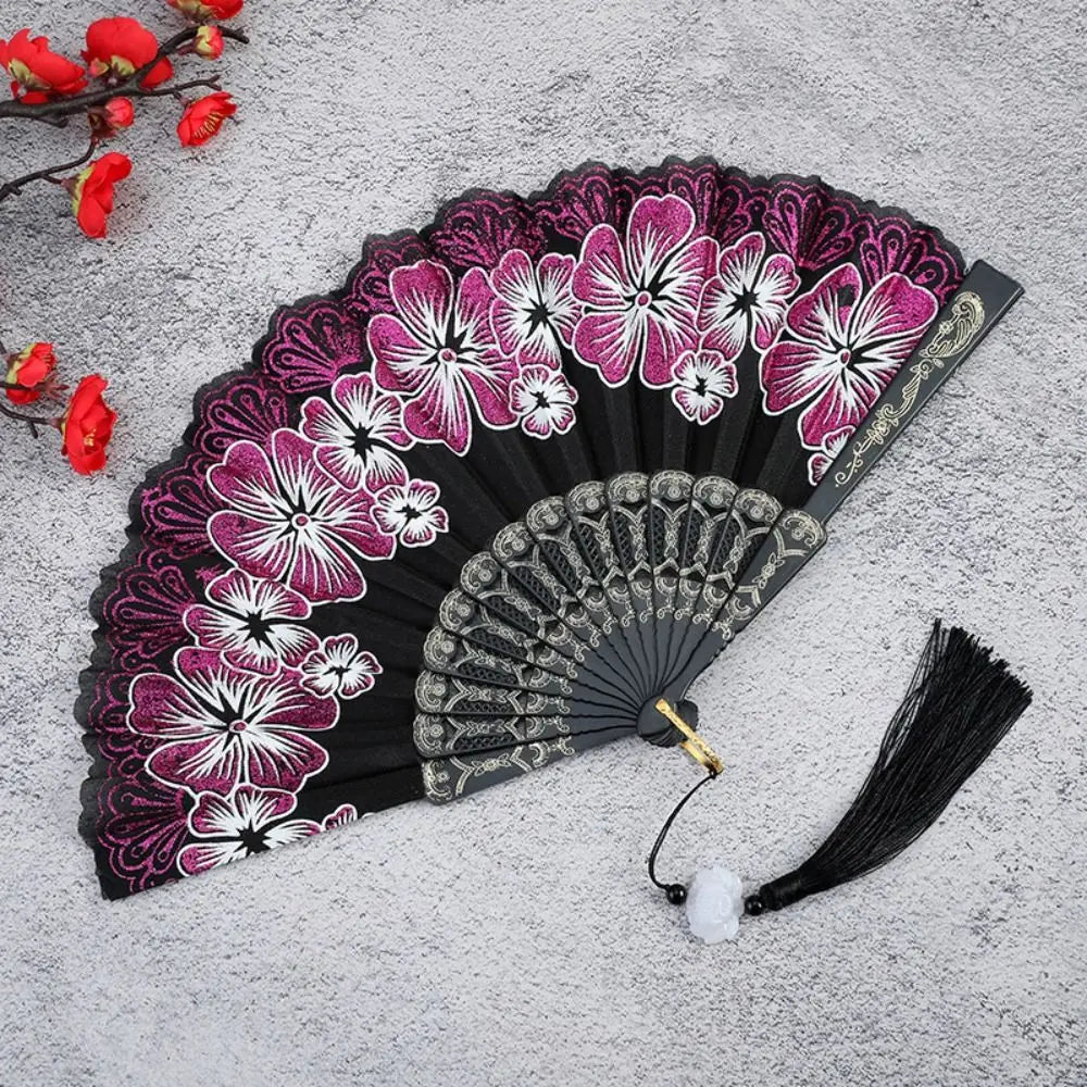 A black folding fan decorated with vibrant pink and white floral patterns on a gray background.