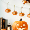 A collection of various orange pumpkin hanging ornaments displayed against a white wall.