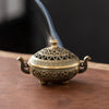 A vintage brass incense burner holder with a lid and spout is shown emitting smoke.