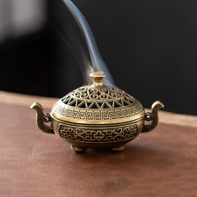 A vintage brass incense burner holder with a lid and spout is shown emitting smoke.