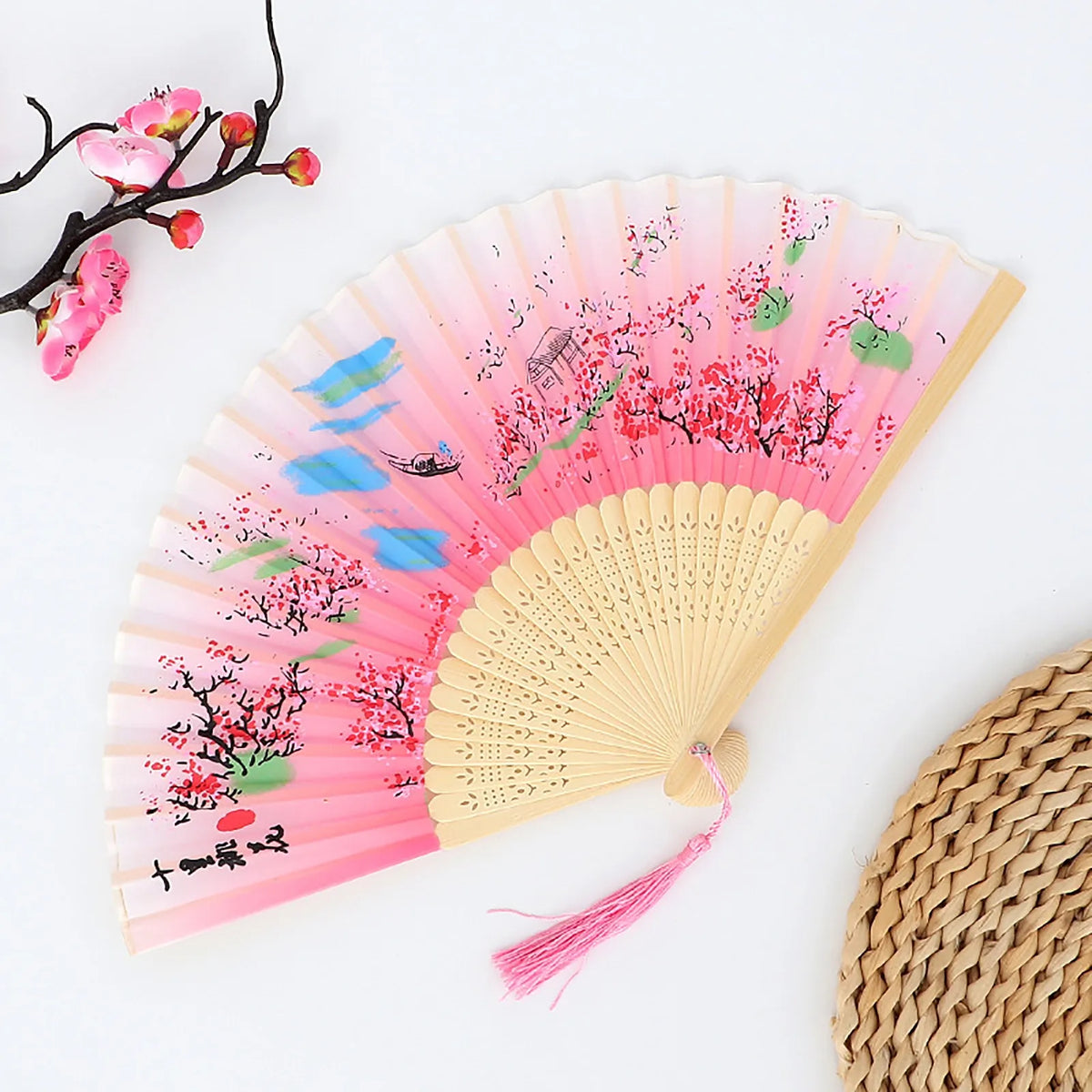 A vintage bamboo folding fan with pink and red fabric featuring floral designs and a light wood frame.