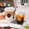 A hand holds a clear disposable coffee cup with a lid, featuring a smile for happiness design.