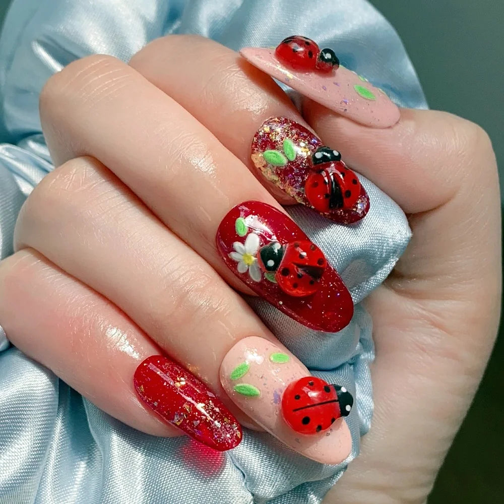 A hand displays various red and black ladybug resin nail art charms on fingernails against a blue fabric background.