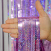 A hand holds a purple metallic foil tinsel fringe backdrop set with iridescent glitter strands.