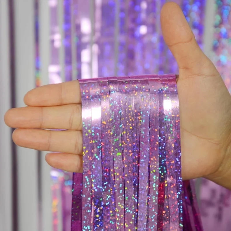 A hand holds a purple metallic foil tinsel fringe backdrop set with iridescent glitter strands.
