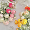 A bouquet of lifelike silk peony flowers in shades of pink, peach, and yellow arranged on a white surface.