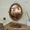 A round wooden vanity mirror with a gold frame and a rotating oval mirror surface.