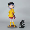 A figurine of a girl with blue hair and a yellow coat and red skirt standing on a base.