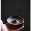 A hand holds a dark brown solid wood incense stick burner bowl against a dark background.