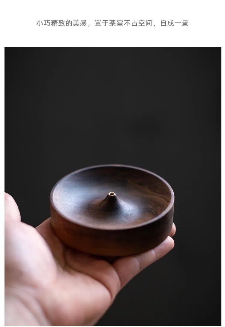 A hand holds a dark brown solid wood incense stick burner bowl against a dark background.