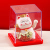 A white lucky cat figurine with a gold crown and red collar is displayed inside a clear red box.