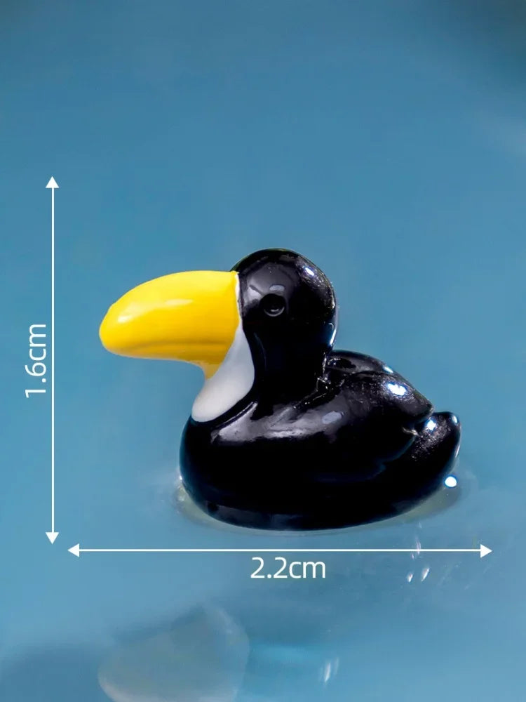 Petite sculpture en résine noire d'un oiseau à bec jaune, sur fond bleu.