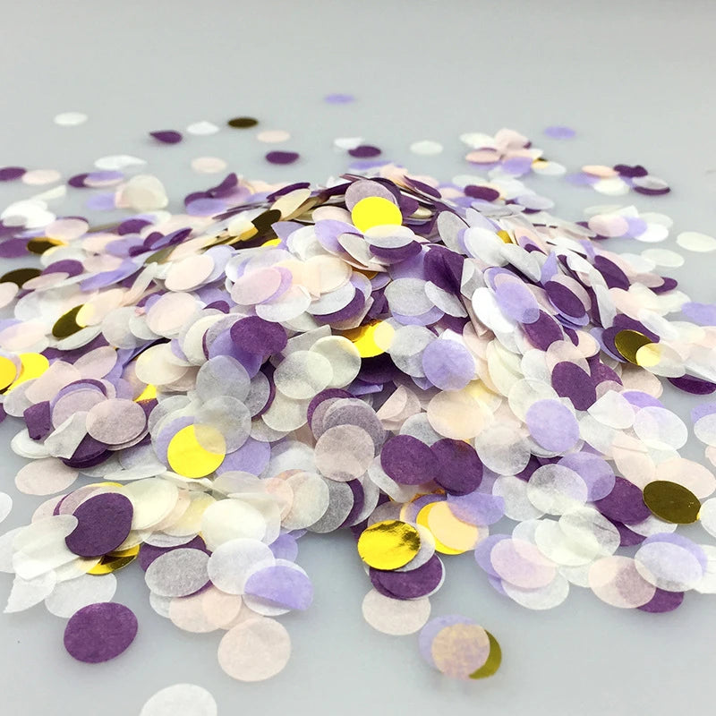 A pile of multicolor paper confetti consisting of purple, white, and gold pieces scattered on a light surface.