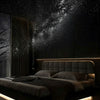 A bedroom scene featuring a bed illuminated by a glowing light, with a starry night sky projected onto the dark wall.