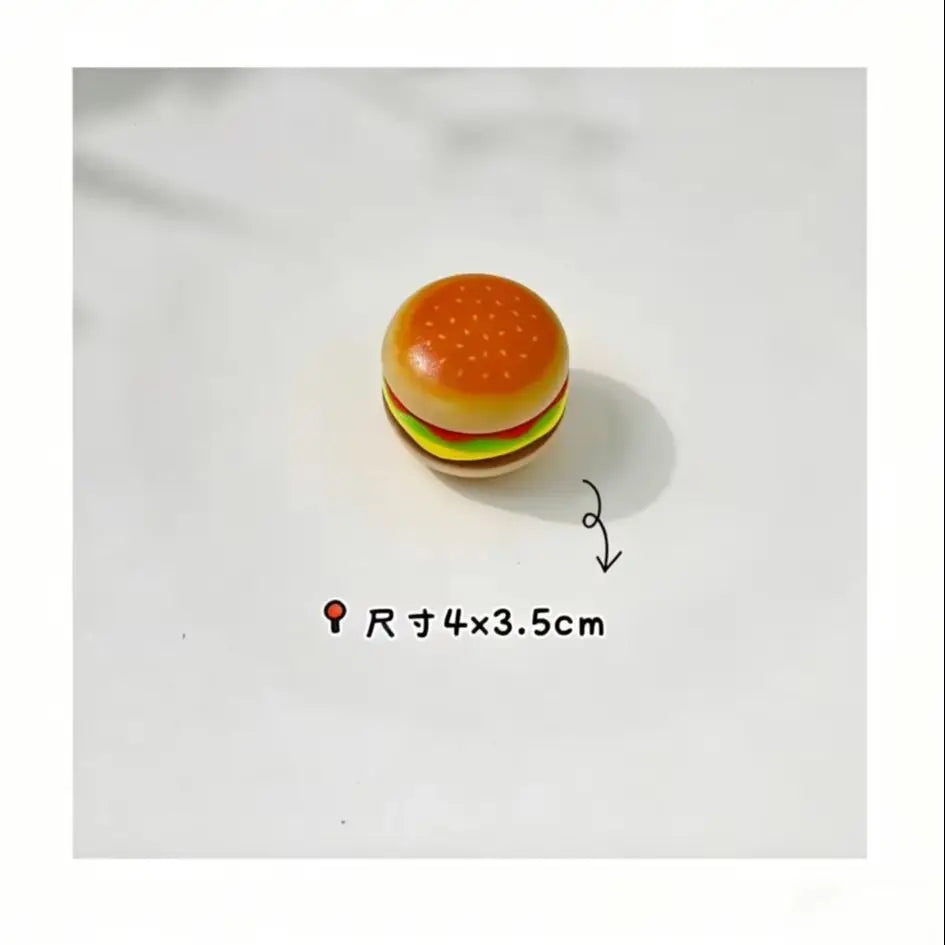 A small, round hamburger-shaped fidget slider toy with an orange bun and green lettuce visible on a white surface.