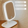 A white LED light makeup mirror is shown on a wooden surface with options for three-color dimming and HD without color.